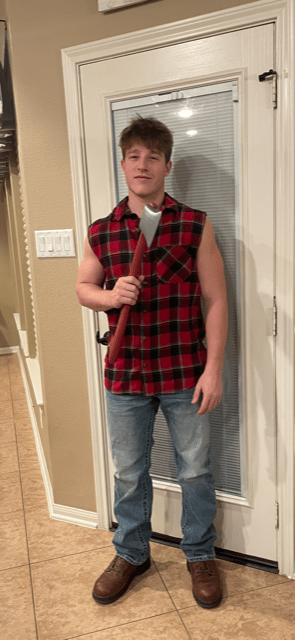 A 2023 photo of Eric dressed as a lumber jack for a Halloween Party. He is holding a toy axe, and is wearing a flannel shirt with the sleeves cut off, blue jeans, and steel-toe boots.