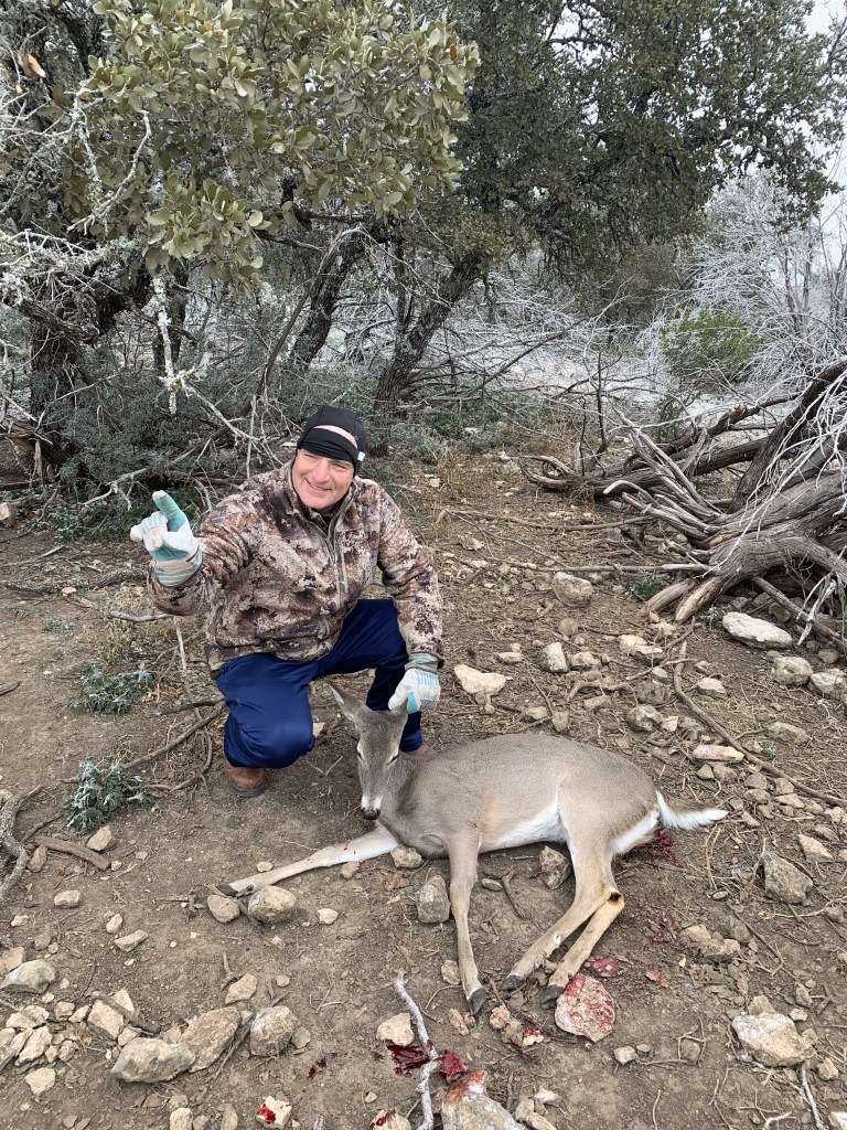 Mike holds up one finger, while knelling down next to a whitetail doe.