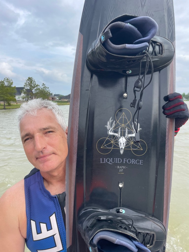 Mike sits on the back of the boat holding his Liquid Force Raph 137 up to the camera's view.