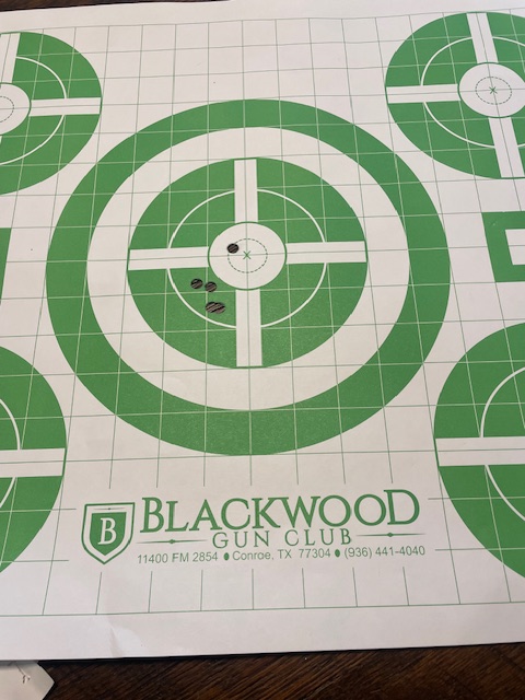 The target shows five shots. All shots are grouped within a four-inch diameter circle. Four of the shots are grouped in a 1.25 inch diameter circle located about 1-inch-low and 1-inch-left of the bullseye.